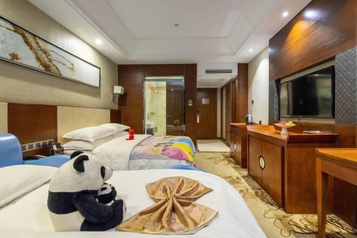 A hotel room with a bed, a desk, a television, and a bathroom visible through an open door.