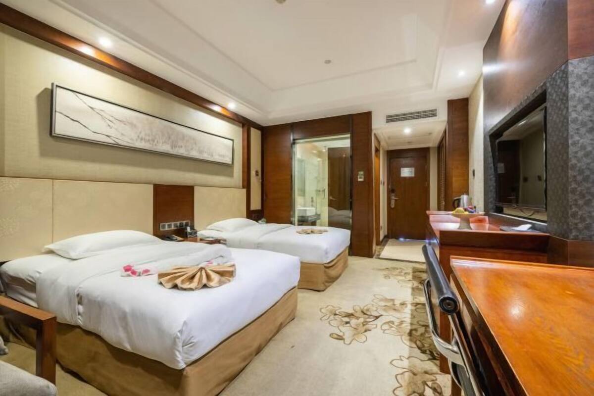 A hotel room with two beds, a television, and a bathroom visible through a glass door.