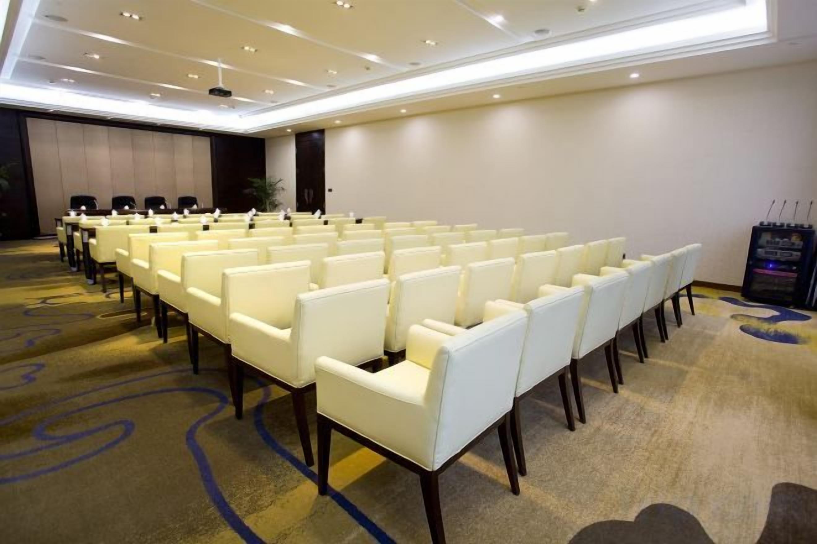 Une salle de conférence avec des rangées de chaises blanches, un sol recouvert de moquette et une estrade.