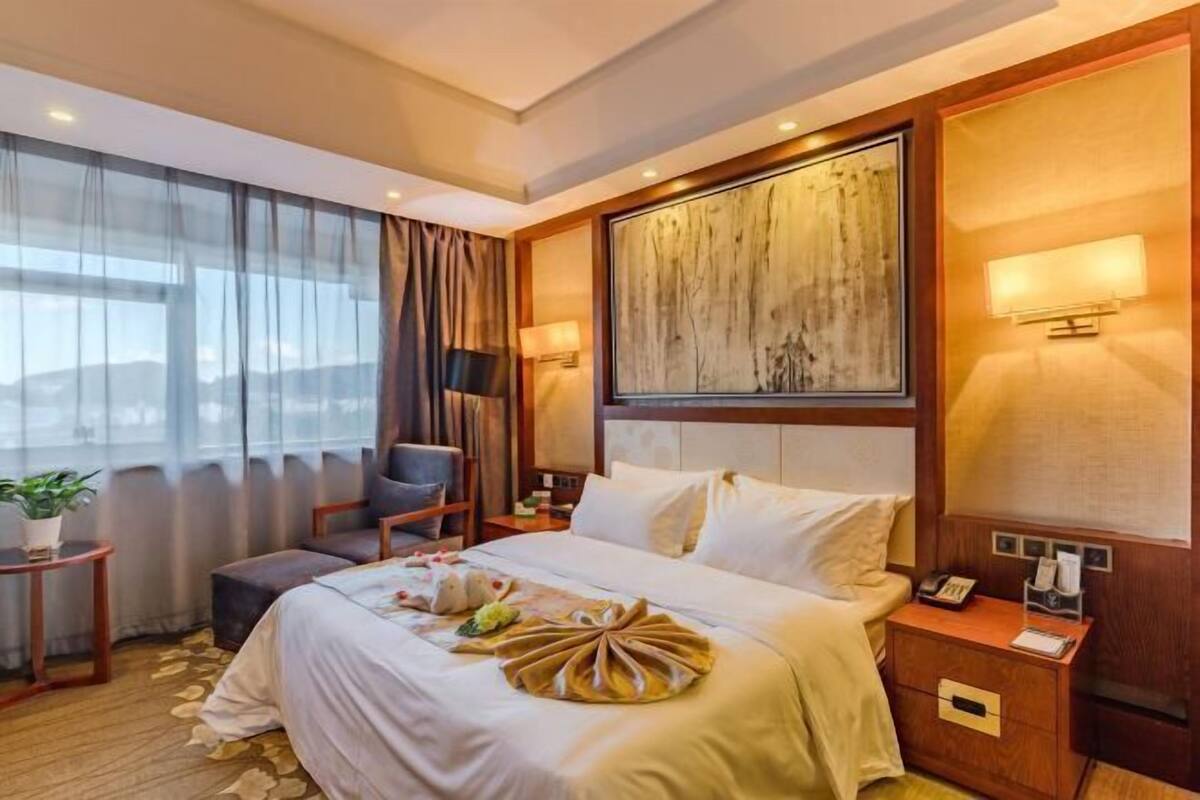 A hotel room with a bed, bedside table, lamp, and a large abstract painting on the wall.