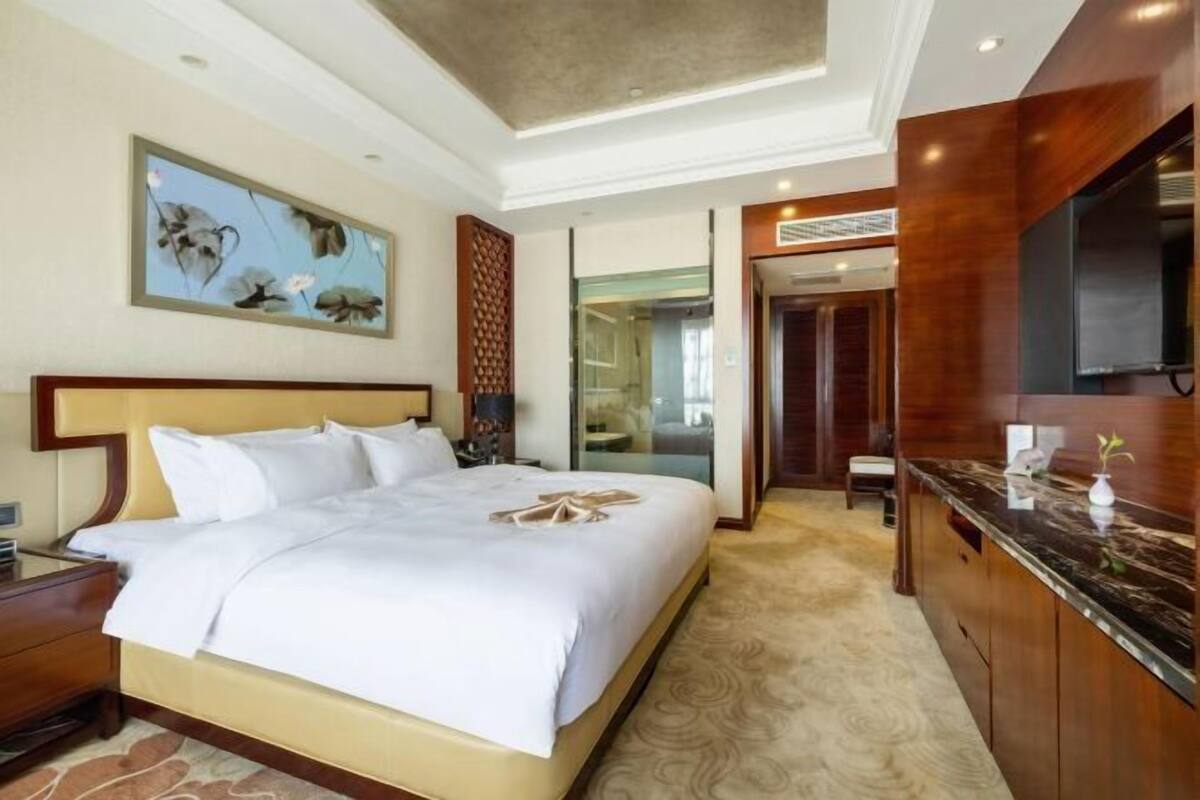 A hotel room with a bed, a desk, a mirror, and a painting on the wall.
