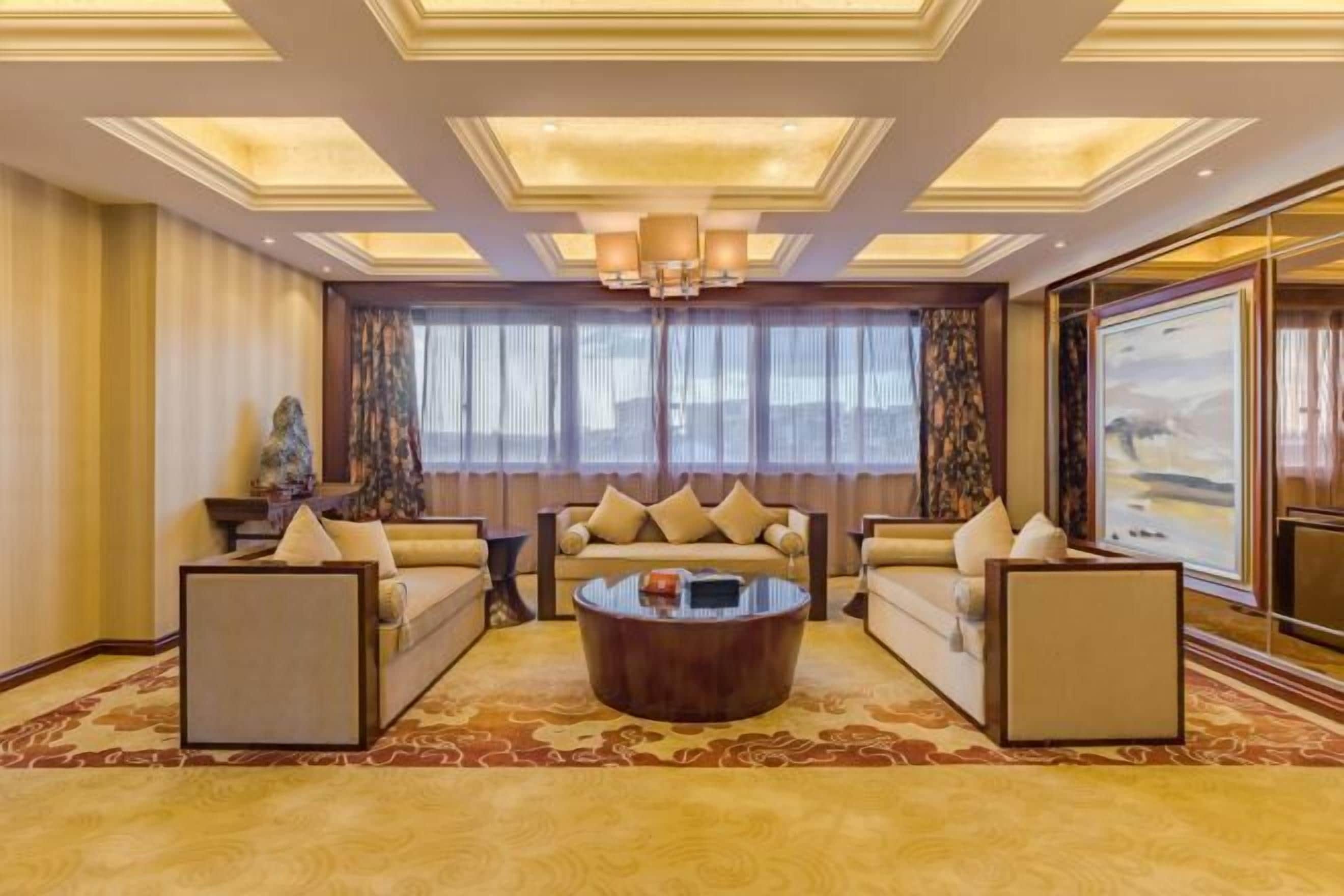 Un salon spacieux comprenant un grand canapé, une table basse et une grande fenêtre agrémentée de rideaux.
