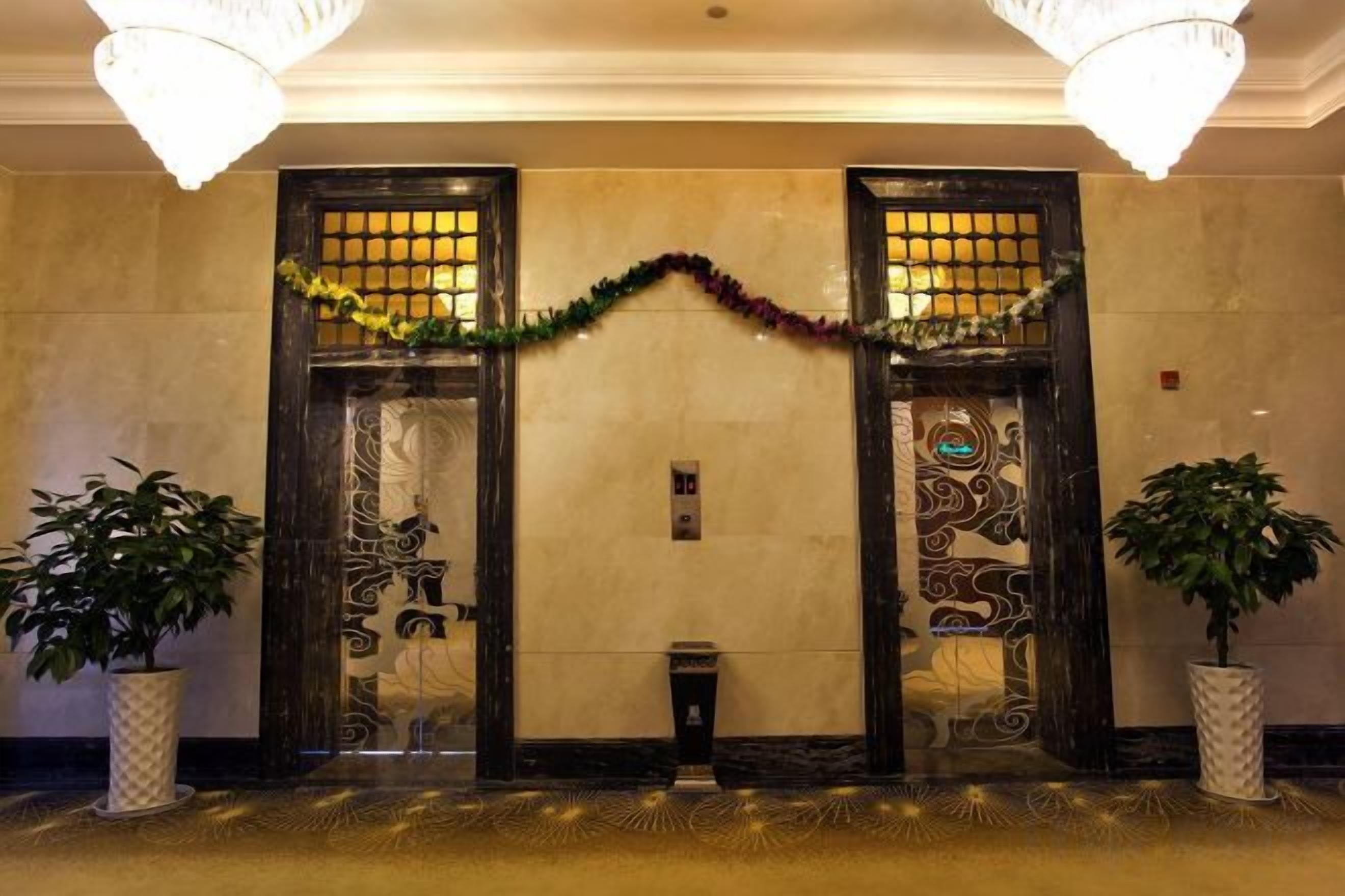 A lobby with two ornate doors, a chandelier, and potted plants.