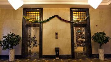 A lobby with two ornate doors, a chandelier, and potted plants.