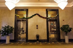 Un vestíbulo con dos puertas decoradas, un candelabro y plantas en macetas.