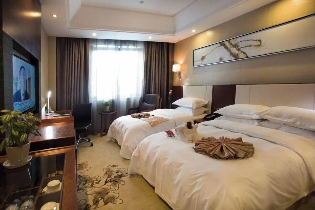A hotel room with two beds, a desk with a computer, a TV, and a plant.