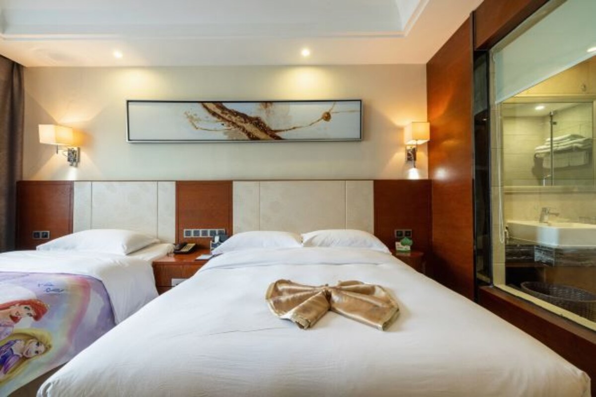 A hotel room with two beds, a large window, a painting on the wall, and a shower visible through the glass.