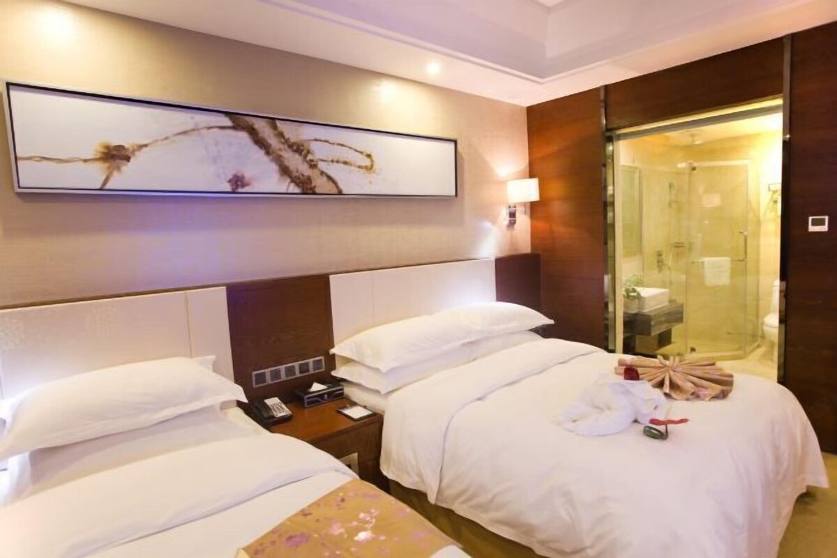 Une chambre d’hôtel avec deux lits, une grande peinture abstraite, une douche en verre et une table de chevet avec une lampe.