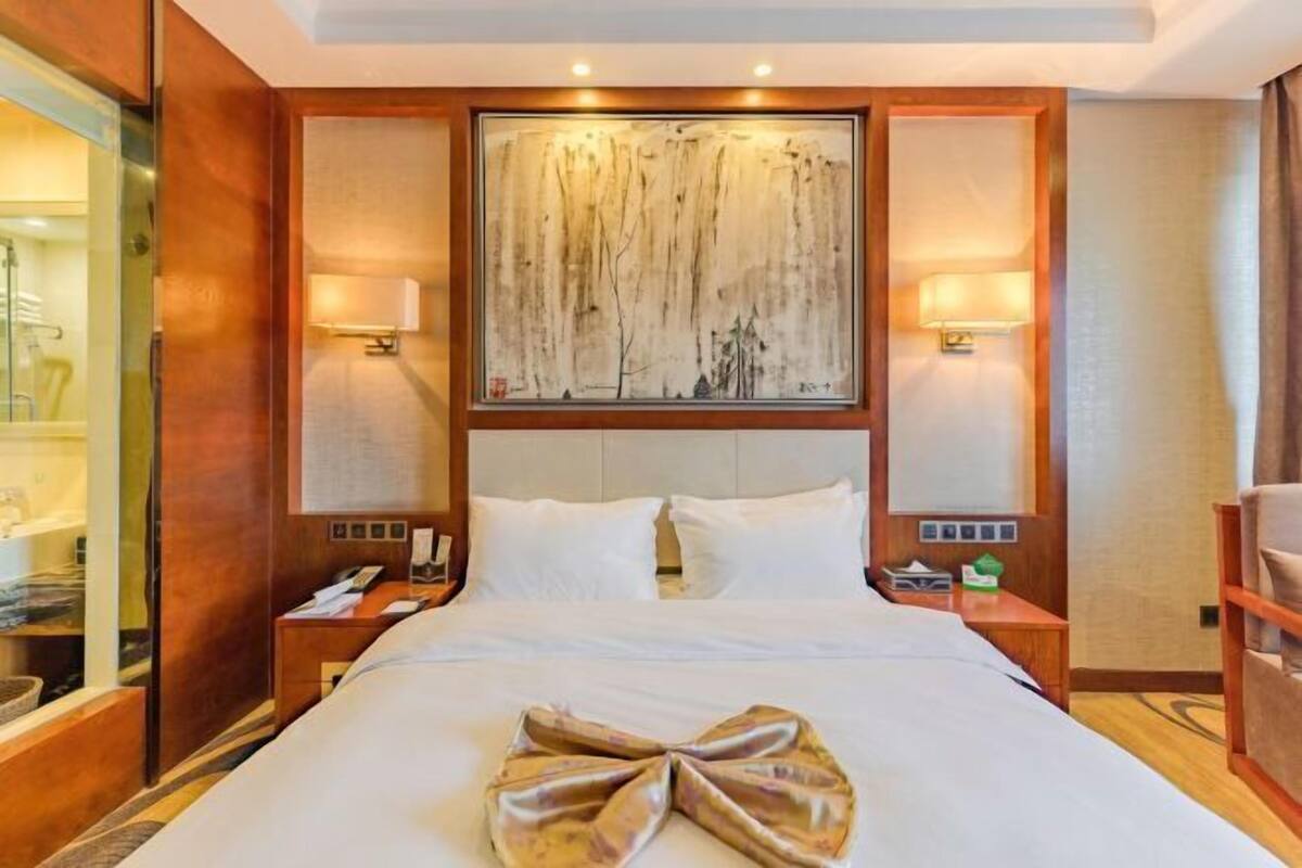 A hotel room with a large bed, two bedside tables, a nightstand, a wall-mounted artwork, and a wooden panel design.