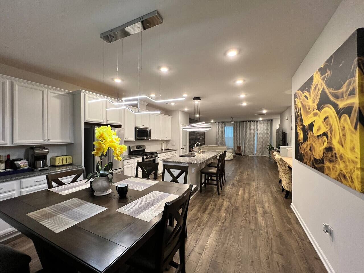 A modern kitchen with white cabinets, a central island, and a dining area with a dark wooden table.
