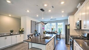 Una cocina moderna con una isla central, armarios blancos y una estufa de acero inoxidable.