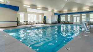 Una piscina interior con agua cristalina, rodeada de ventanas y sillas.