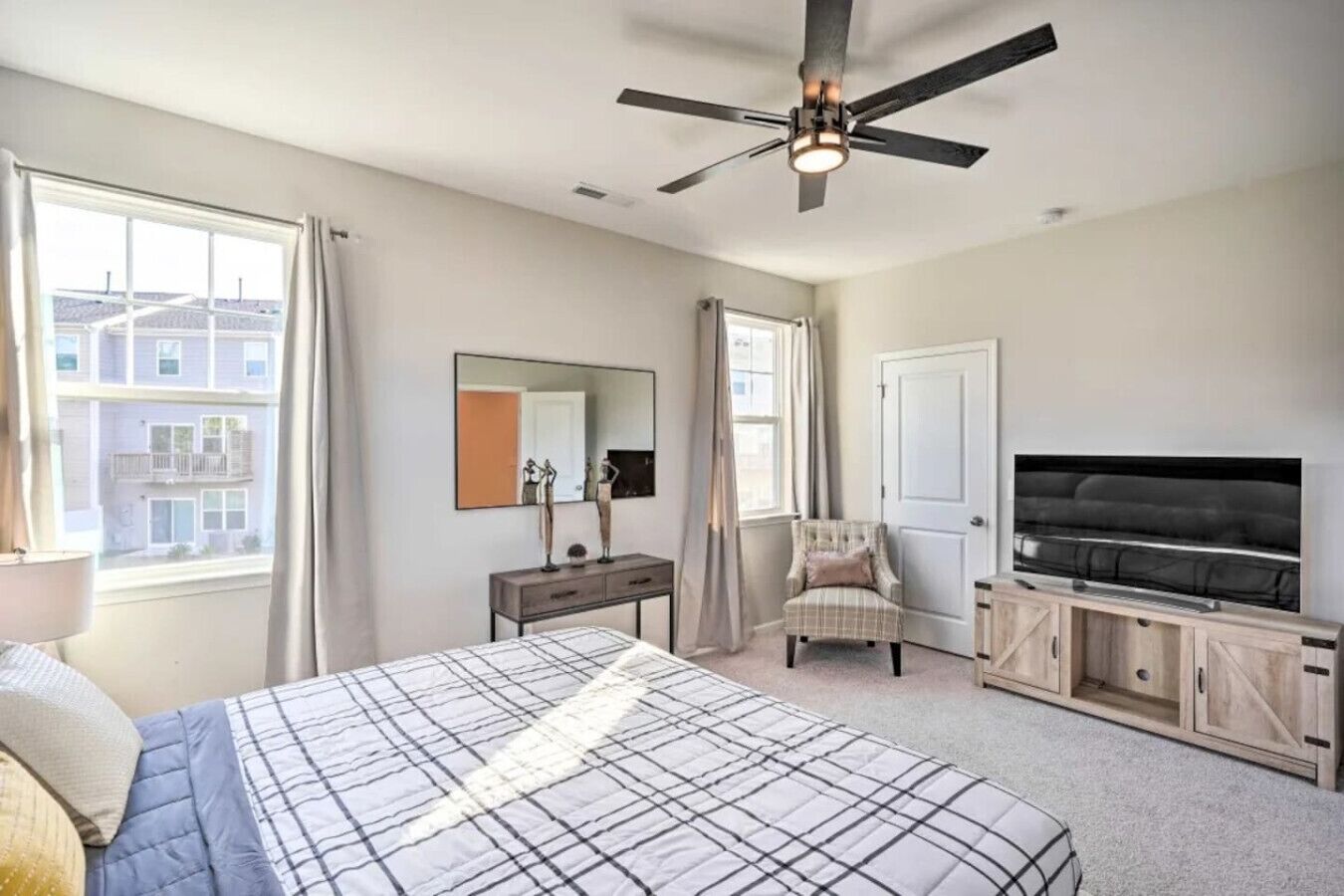 A bedroom with a bed, a desk, a chair, a TV, and a ceiling fan.