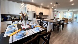 Una cocina moderna con armarios blancos, una isla central y una zona de comedor preparada para seis personas.