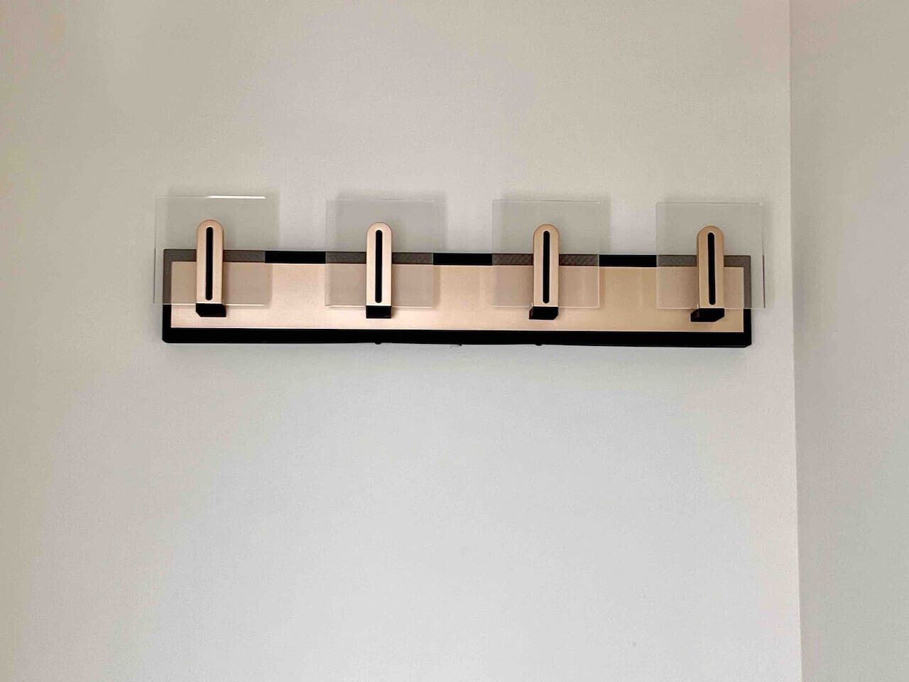 A wall-mounted, rectangular, metallic object with three vertical slots, likely a coat rack, against a plain wall.