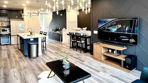 A modern kitchen with a central island, a dining area with a TV, and a living space with a coffee table. - TPV - Antilia - Luxury w/Indoor Heated Pool & Gym (Durham)