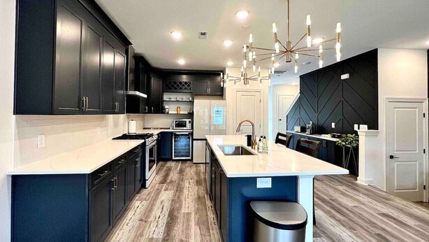 A modern kitchen with dark cabinetry, a central island, and a chandelier. - TPV - Antilia - Luxury w/Indoor Heated Pool & Gym (Durham)