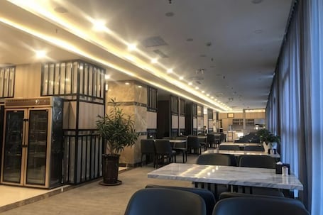 A modern hotel lobby with marble flooring, a reception desk, and a seating area with tables and chairs.. Junrui Garden Hotel