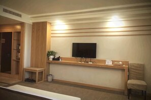 Un'area reception con una TV a schermo piatto, una scrivania in legno, un piccolo angolo salotto e un cestino.