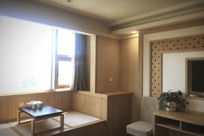 A room with a tatami mat seating area, a small table, a television, and a plant. - Junrui Garden Hotel (Qianguo)