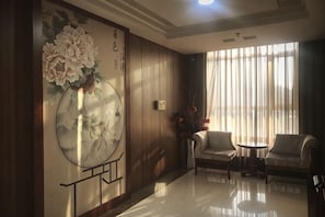 A room with wooden paneling, a round mirror, two chairs, a small table, and a large window with curtains.