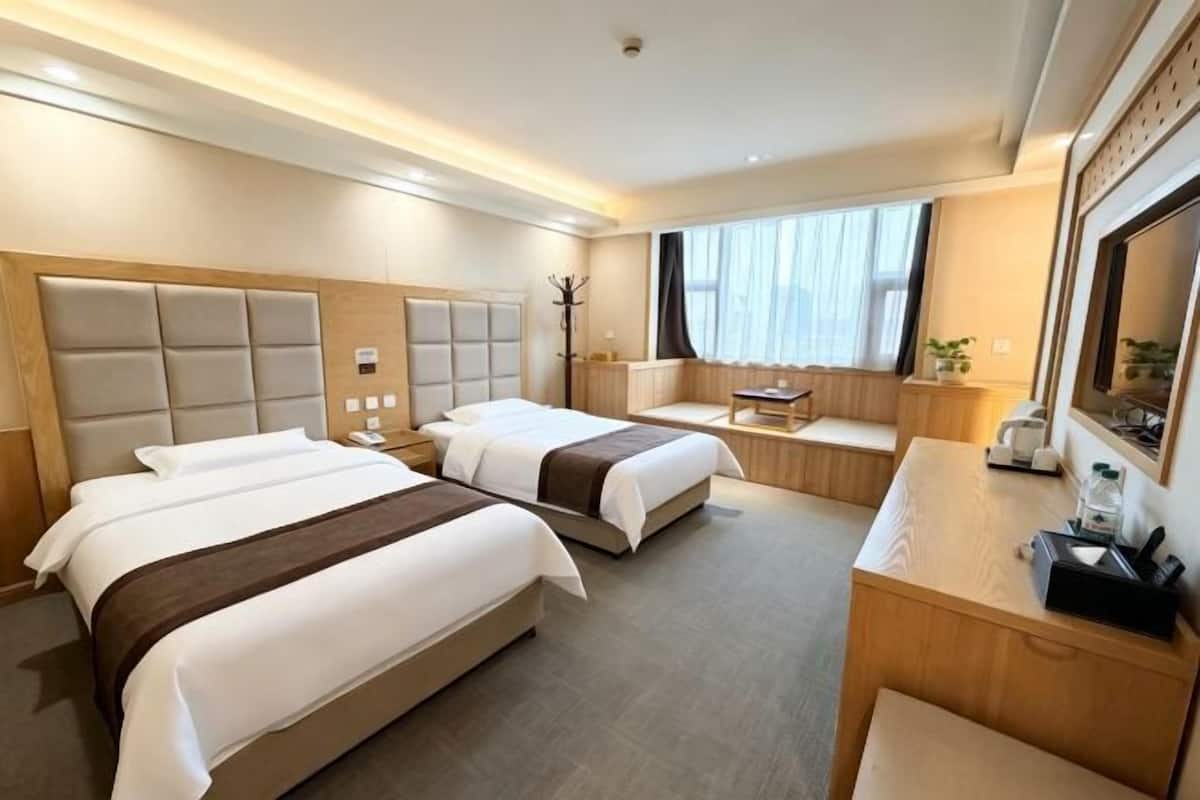Ein Hotelzimmer mit zwei Betten, einem Schreibtisch, einem Stuhl, einem Kleiderständer und einem großen Fenster.