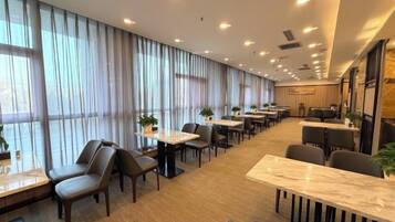 A hotel dining area with long tables, chairs, and large windows.