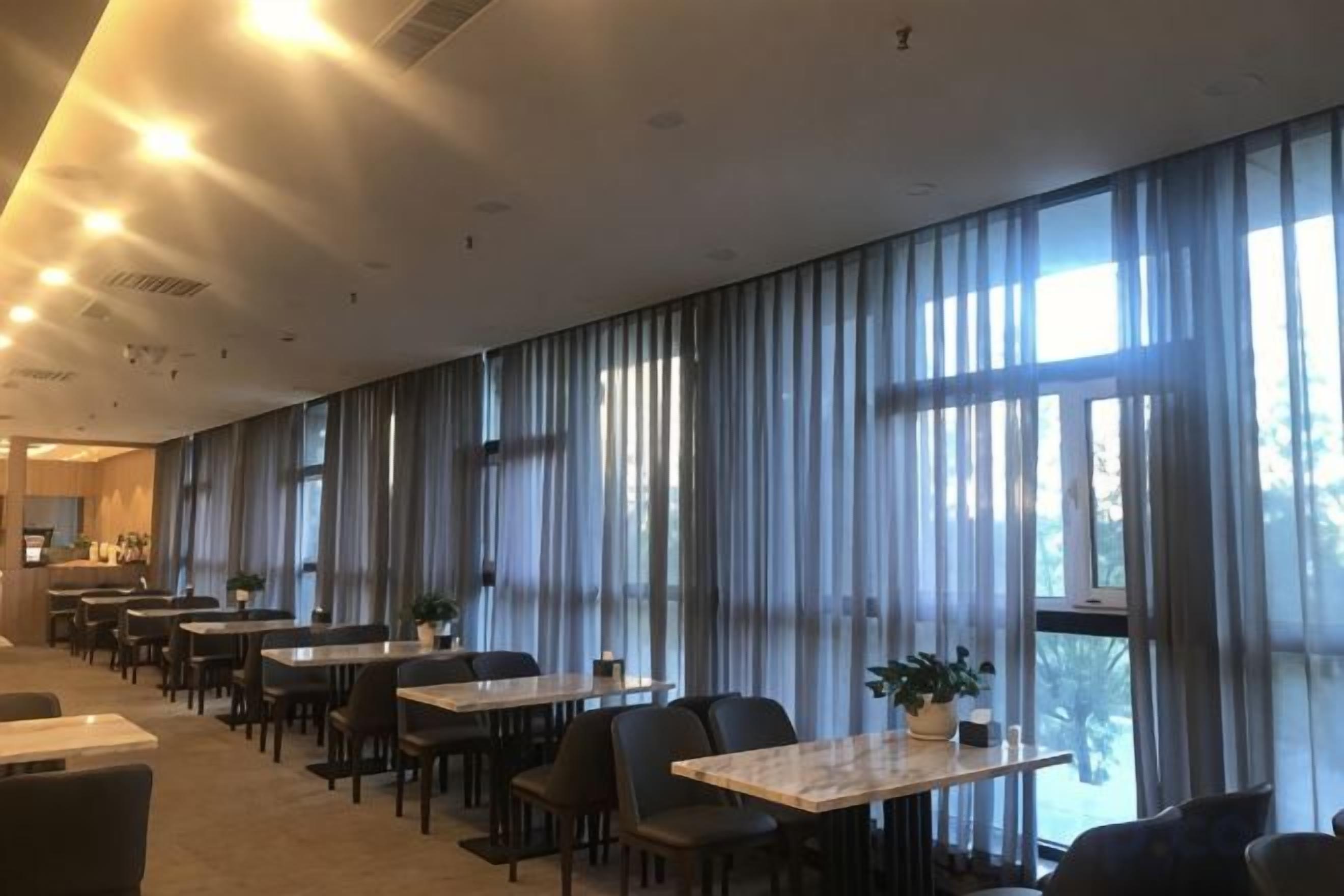 A hotel dining area with long tables, chairs, and large windows with curtains.