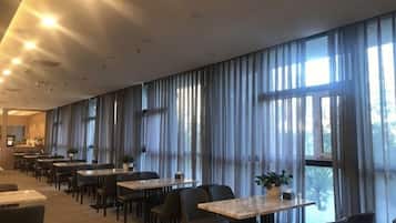 A hotel dining area with long tables, chairs, and large windows with curtains.