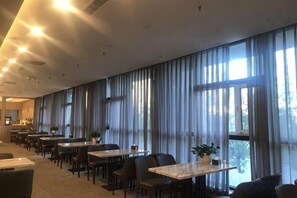 A hotel dining area with long tables, chairs, and large windows with curtains. - Junrui Garden Hotel (Qianguo)
