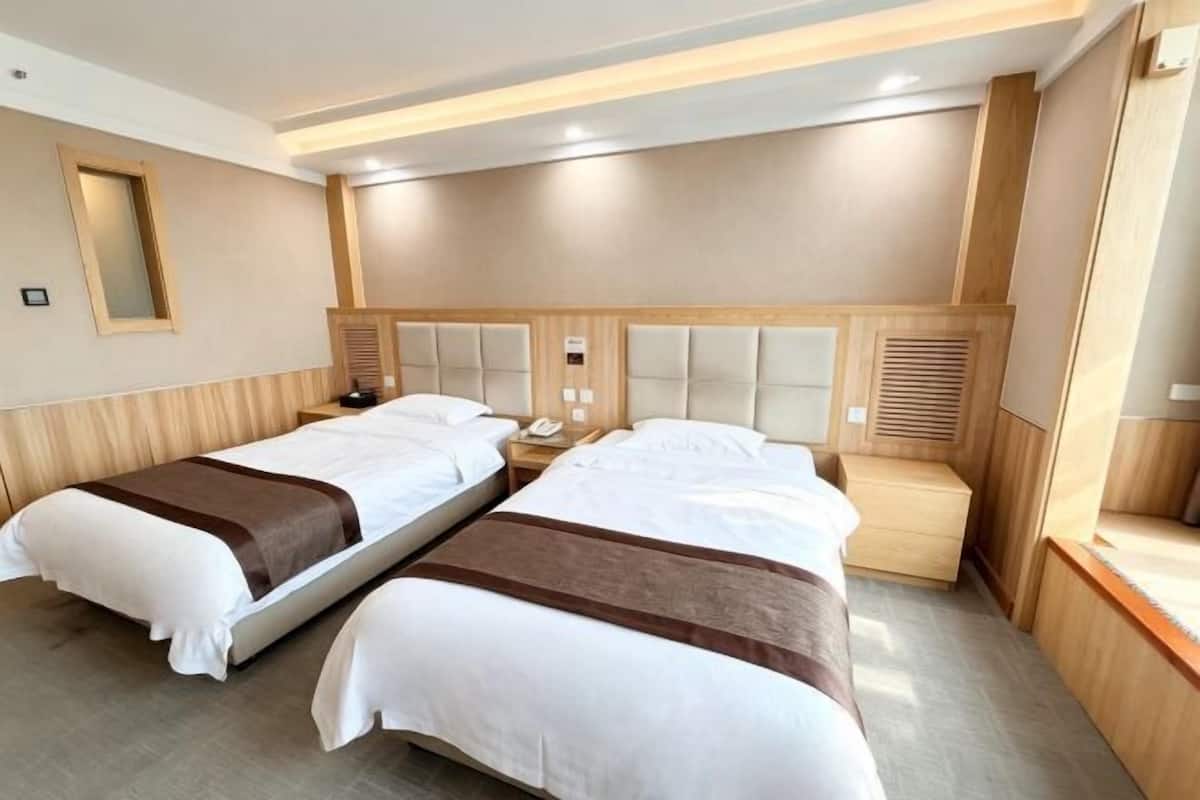 Ein Hotelzimmer mit zwei Betten, Holz-Kopfteilen, Nachttischen, einem Spiegel und einer fest installierten Heizung.