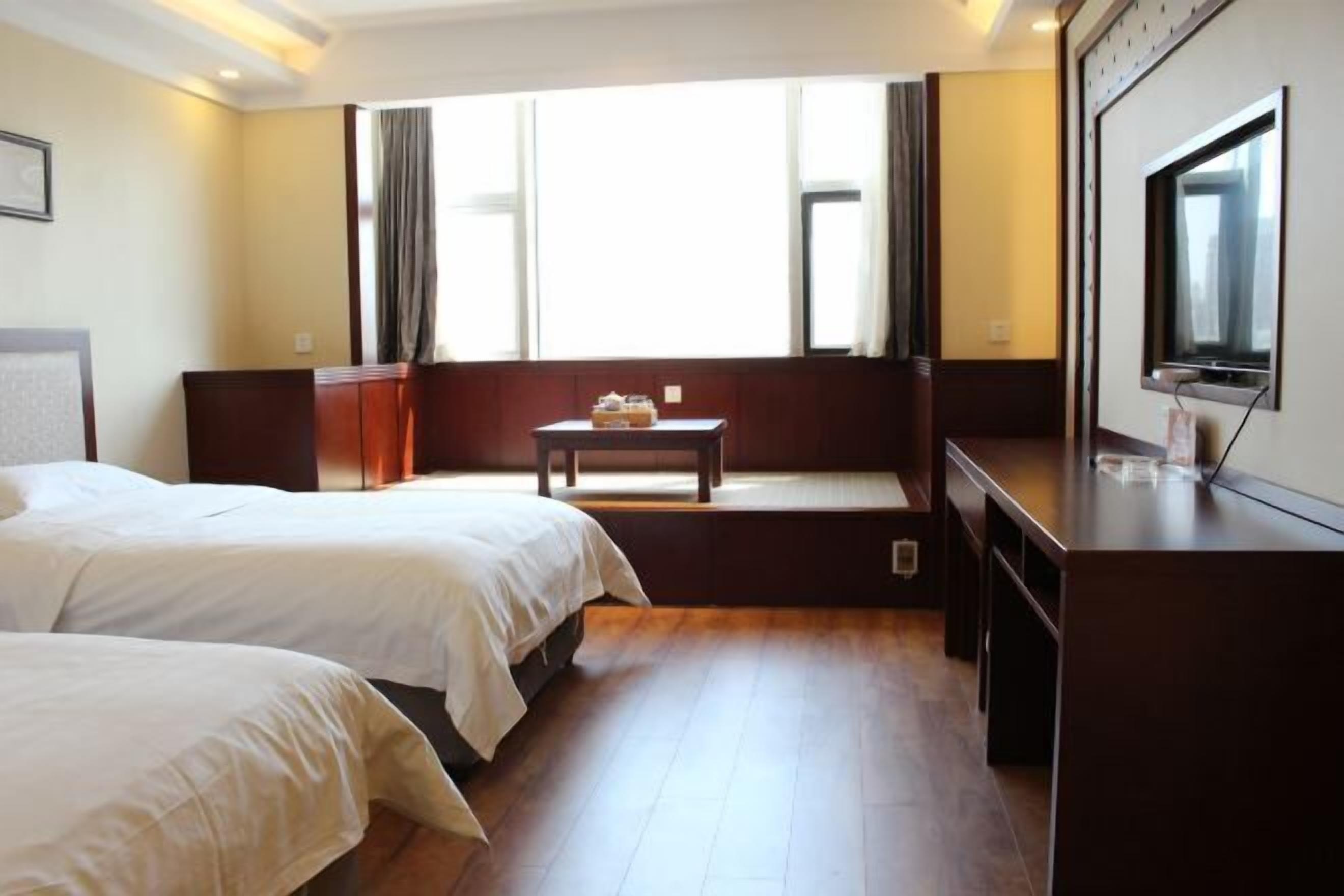 A hotel room with two beds, a small table, a TV, and a window with curtains.