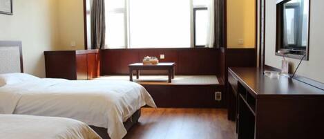 A hotel room with two beds, a small table, a TV, and a window with curtains.