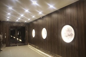 Un pasillo con paneles de madera, apliques de pared circulares y un suelo reflectante.