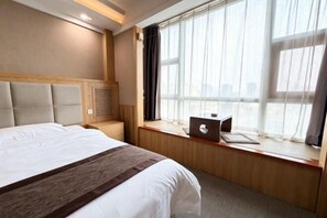 A hotel room with a bed, a window with curtains, a laptop on the windowsill, and a wooden headboard. - Junrui Garden Hotel (Qianguo)