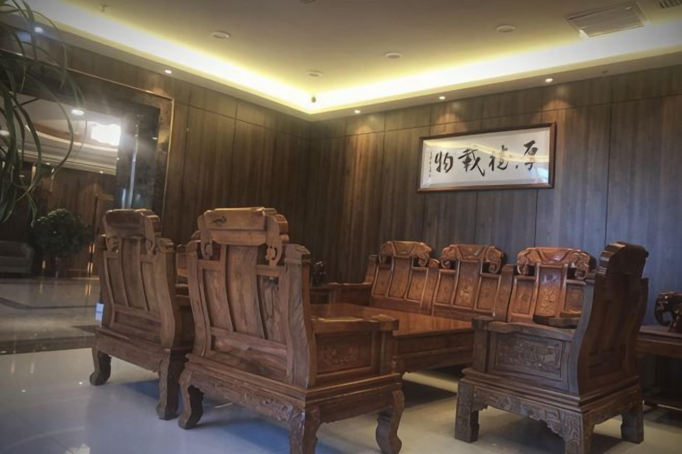 A traditional wooden sofa set in a room with dark wooden walls and a framed calligraphy piece on the wall.