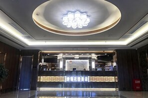 A hotel reception area with a modern design, a reception desk, and a decorative ceiling light fixture. - Junrui Garden Hotel (Qianguo)