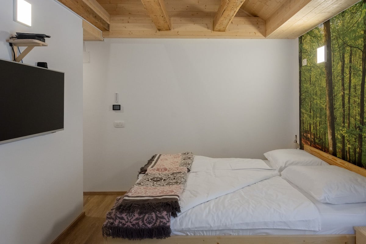 Une chambre à coucher avec un lit, un téléviseur fixé au mur et une fresque murale sur le thème de la forêt.