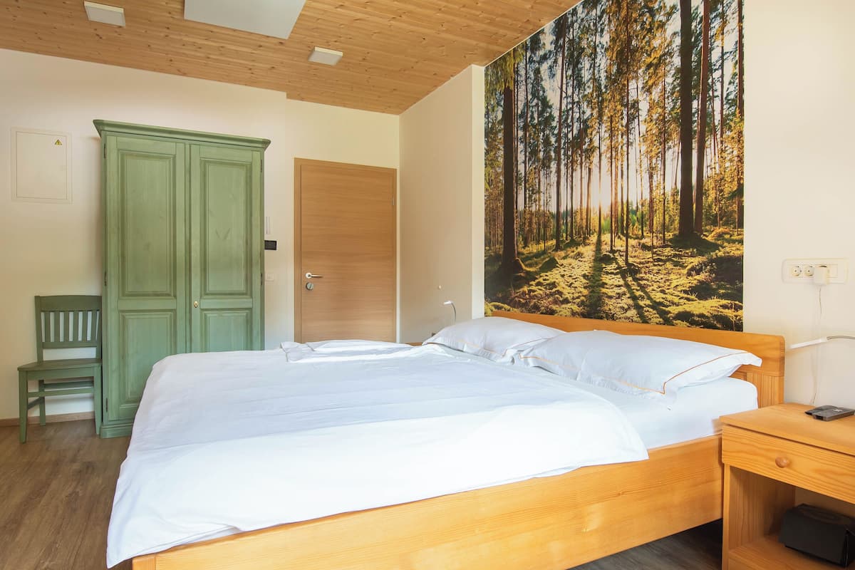 Une chambre avec un lit en bois, une armoire verte, un banc et une fresque murale représentant une forêt.