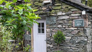 A stone house with a white door, a sign reading "Little How," and a potted plant in front. - Little How (Ambleside)