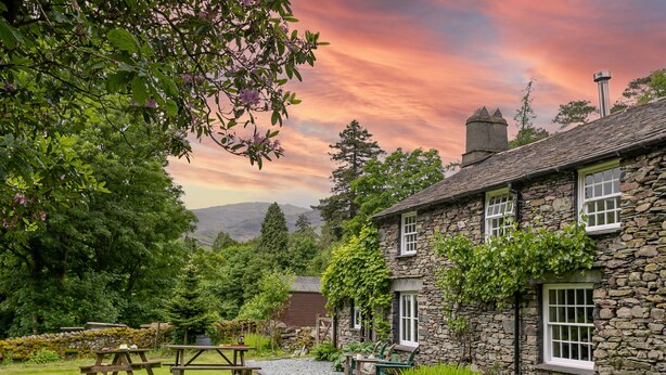 A stone building with a garden, picnic tables, and a view of hills. - Little How (Ambleside)