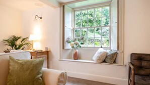 A cozy living room with a large window, a sofa, a chair, a lamp, and a small table with a plant. - Little How (Ambleside)