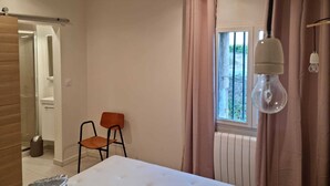 Un dormitorio con cama, ventana con cortinas, una silla y un radiador.