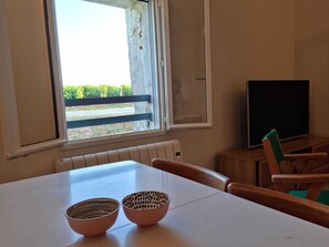 Una habitación con una mesa blanca, dos cuencos, un radiador, un televisor y una ventana con vistas a la vegetación.