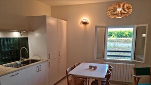 Una cocina moderna con armarios blancos, un lavamanos de acero inoxidable y un comedor con mesa blanca y sillas de madera.