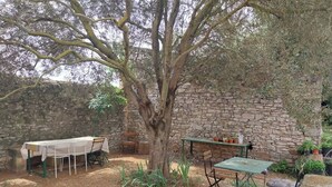Un área de estar al aire libre con un muro de piedra, una mesa con mantel blanco y un árbol.