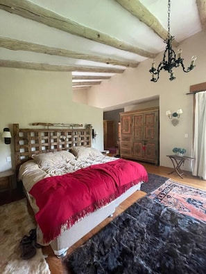 A bedroom with a wooden headboard, a large bed with a red blanket, a black rug, and a chandelier.