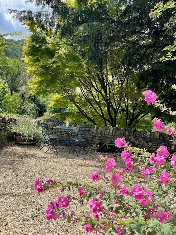 Un jardín con un muro de piedra, una mesa de madera y sillas.