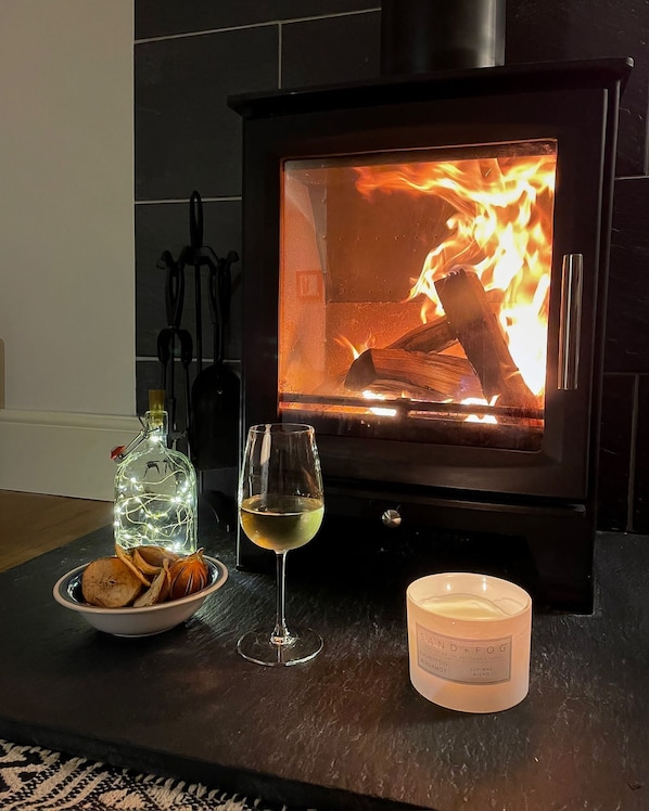 A cozy room with a wood-burning stove, a glass of white wine, a candle, and a bottle of liquor on a table.