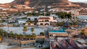 A resort with a swimming pool, palm trees, and a mountainous backdrop.